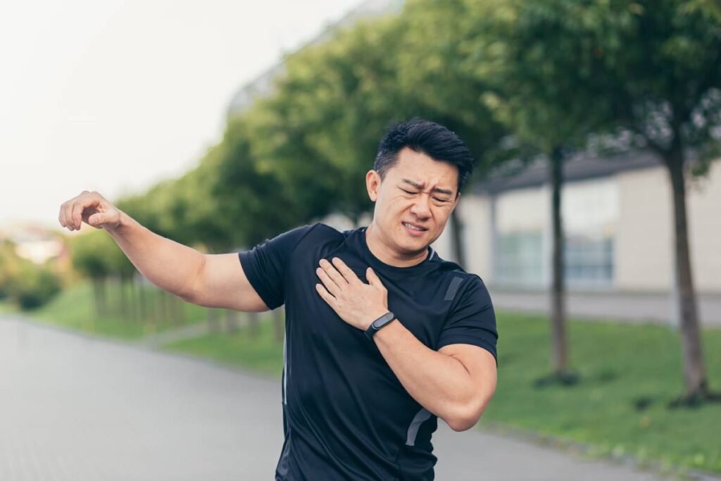 Male asian athlete, kneading shoulder pain, sore arm muscles in the park