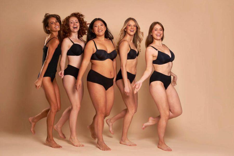 Group of cheerful women in black underwear standing and smiling towards the camera